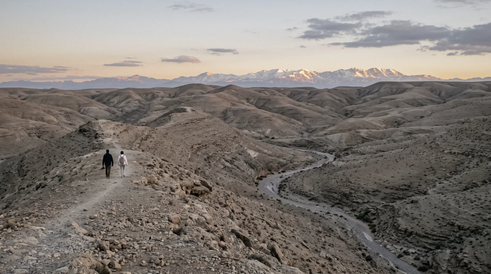 Bare grey-ochre hamada hills folding to the Atlas snowline in the last sun, Agafay desert near Marrakech
