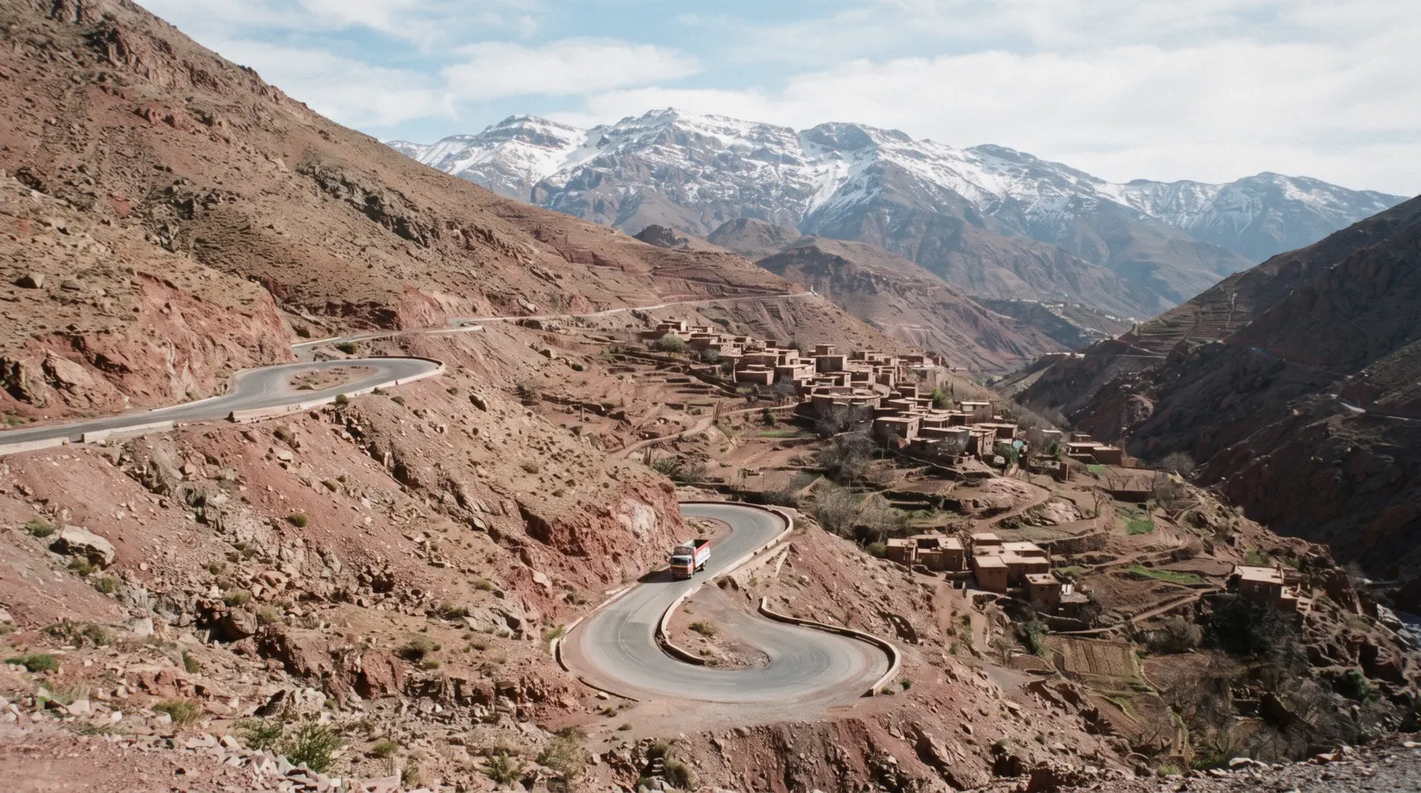 The Tizi n'Tichka road switching back down a bare red ridge with snow on the peaks behind, Atlas Mountains south of Marrakech