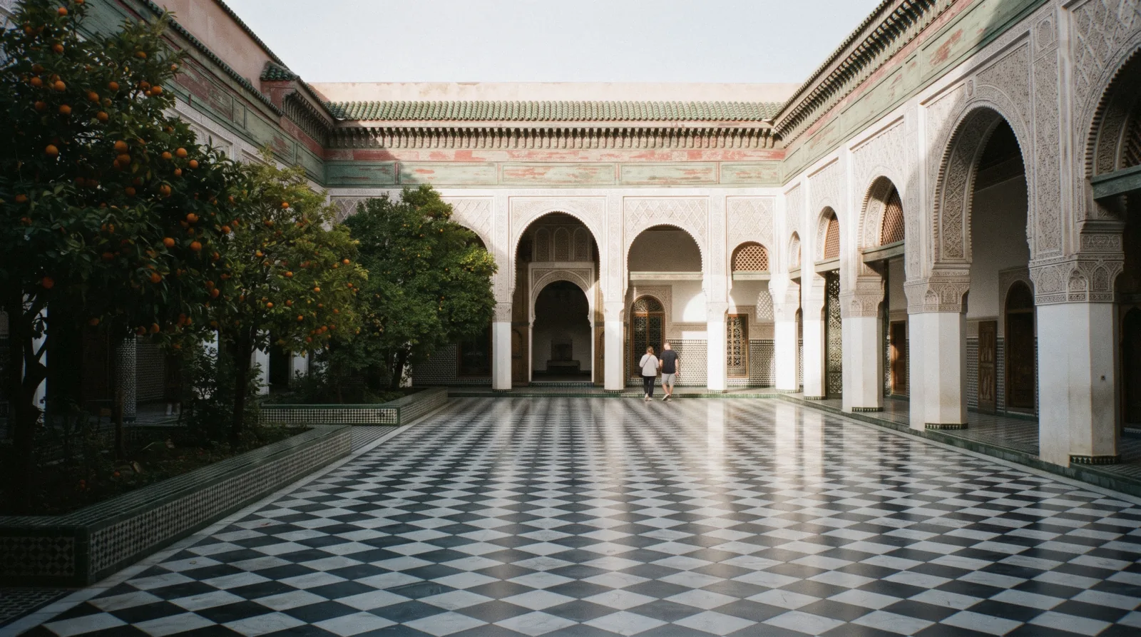 Marble-paved grand courtyard with painted cedar eaves and orange trees at the Bahia Palace in Marrakech, morning shade on one side