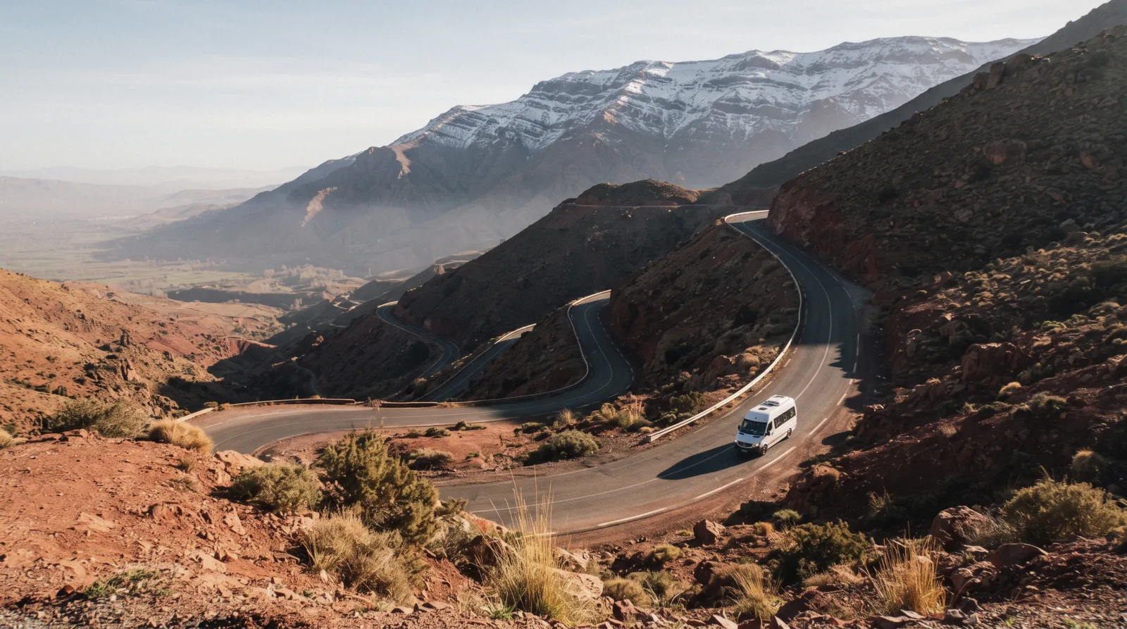 A road climbing out of the plain toward the High Atlas ridgeline under morning light on a day trip from Marrakech