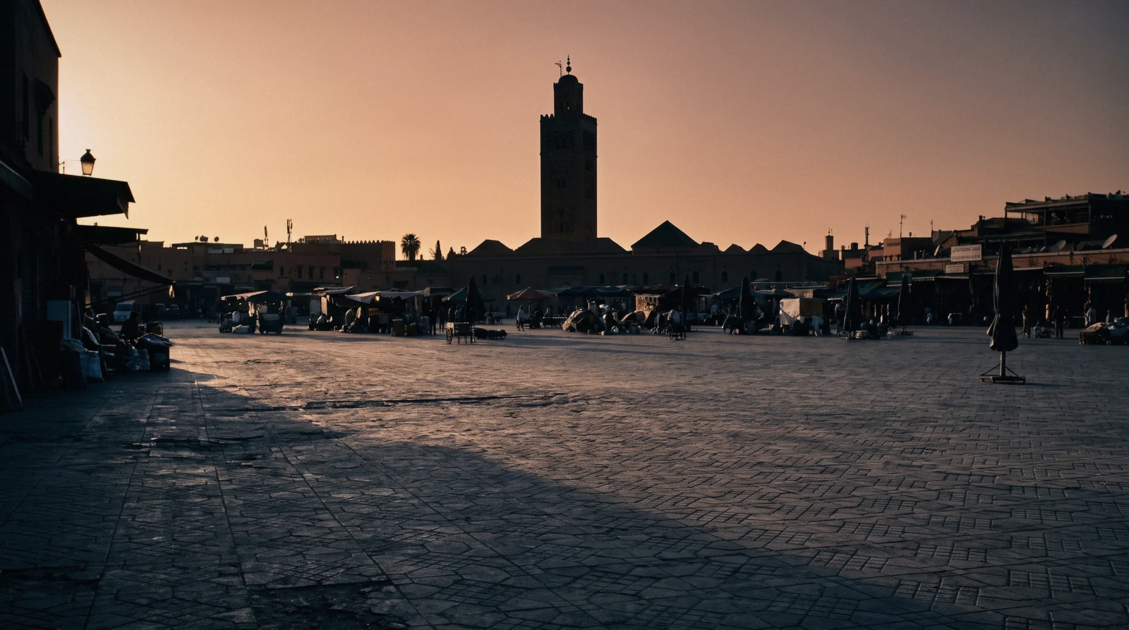 Jemaa el-Fna half in shade and half in low sun with stalls being wheeled into place and the Koutoubia behind, the view that answers whether Marrakech is worth visiting